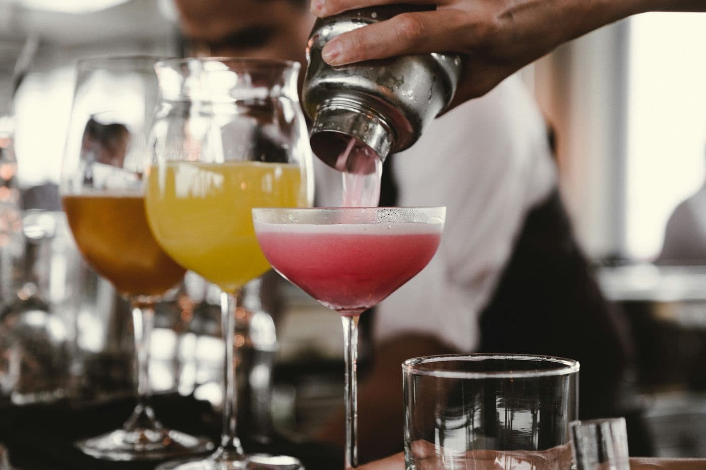Bartender pouring a pink cocktail from a shaker next to other colourful cocktails