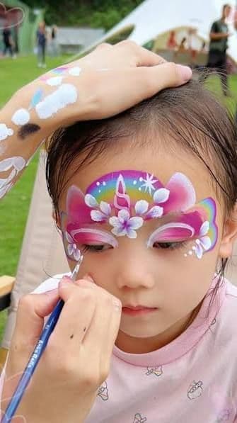 Little girl having a unicorn design with a rainbow and flowers painted on her face