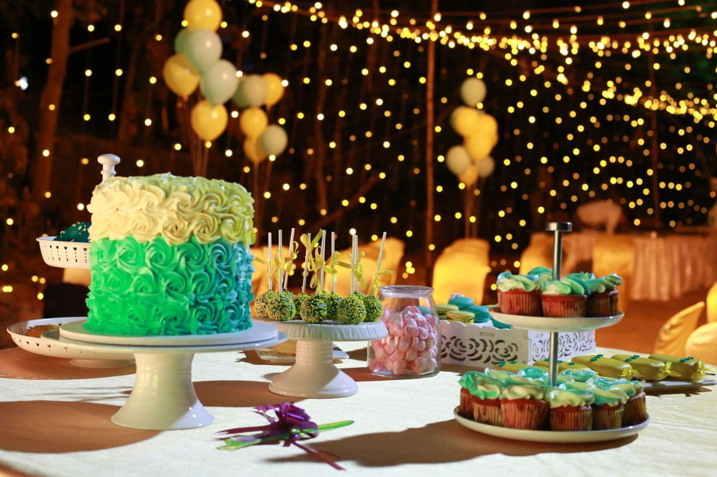 Table de desserts avec gâteau à la crème, cake pops et cupcakes sous des guirlandes lumineuses