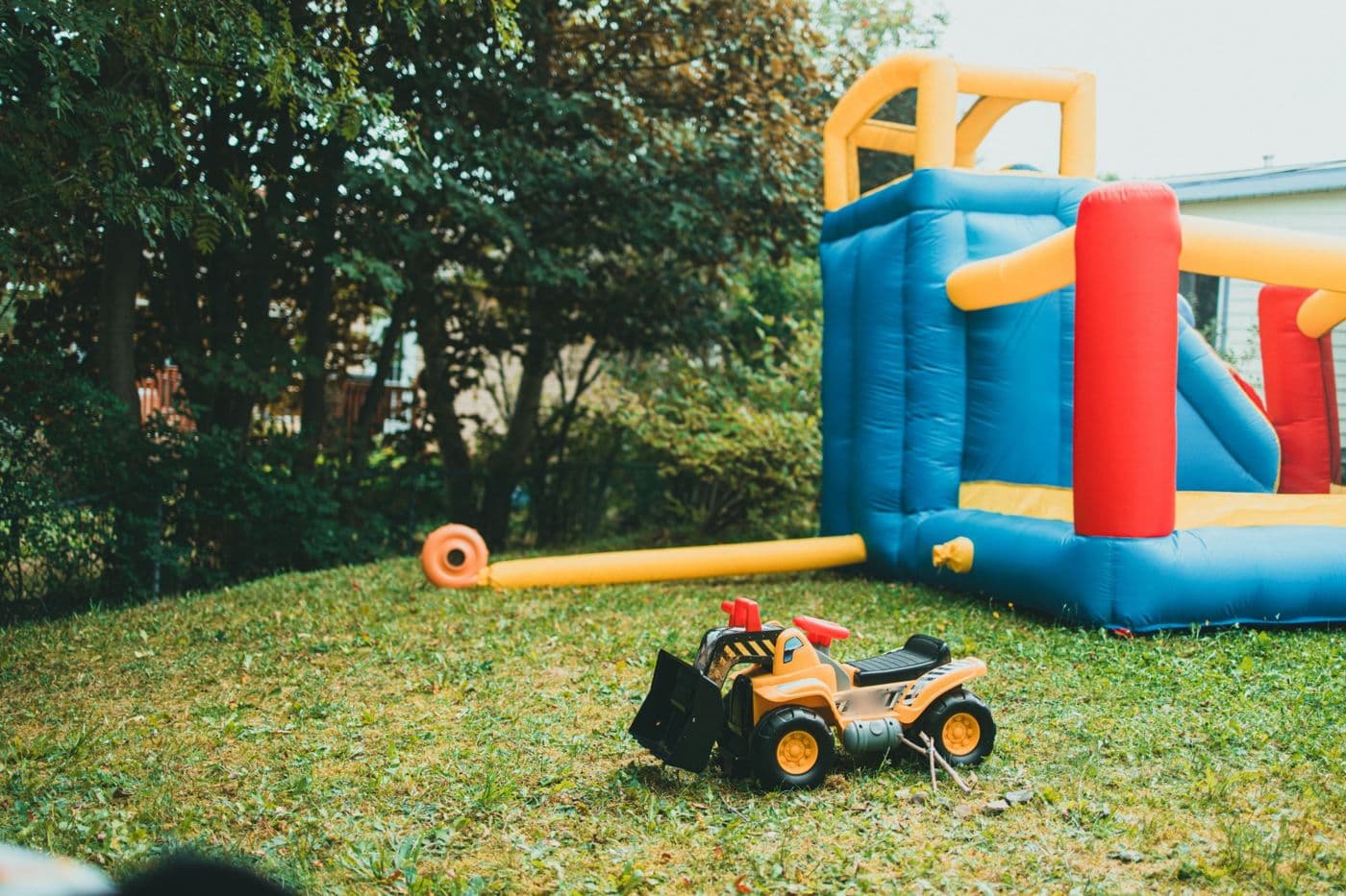Blue, red and yellow bouncy castle in a garden, with a toy tractor on the grass