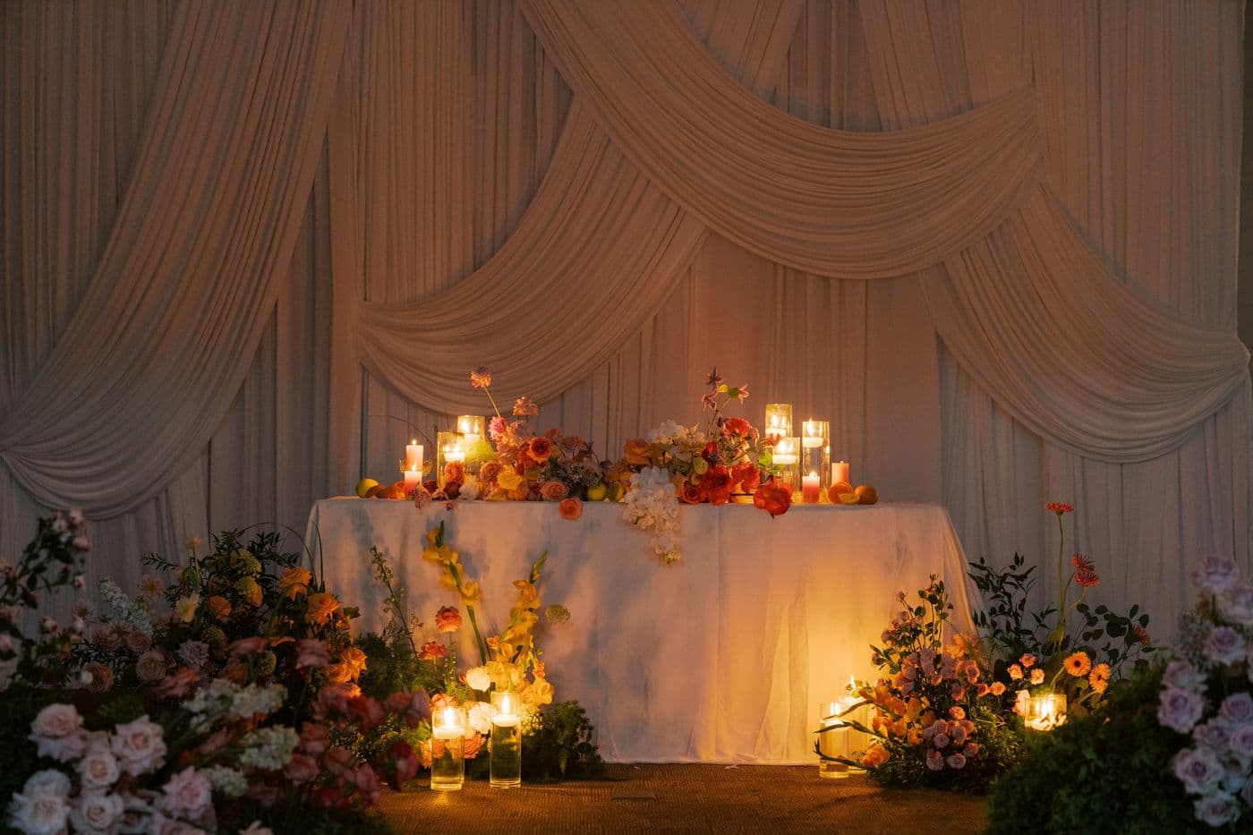 Head table decorated with flowers and candles in front of draped fabric