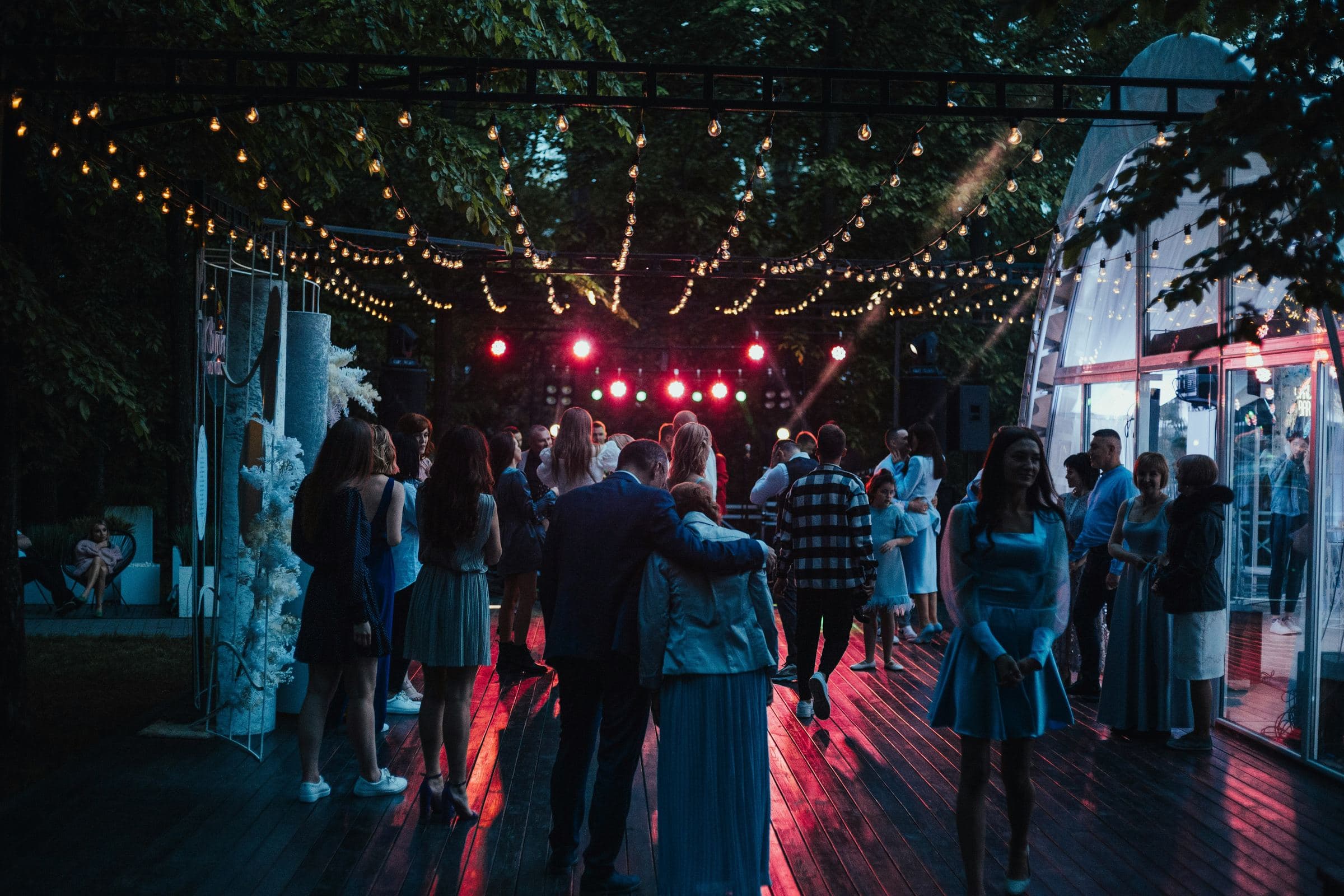 Guests on an outdoor dance floor under string lights at an evening party