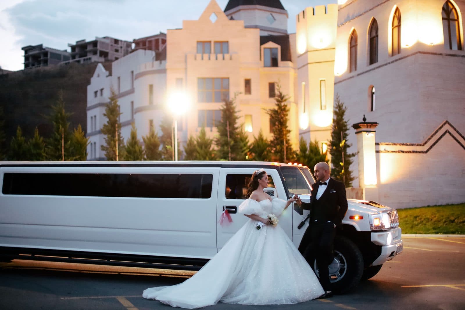 Bride and groom beside a white limousine outside a castle