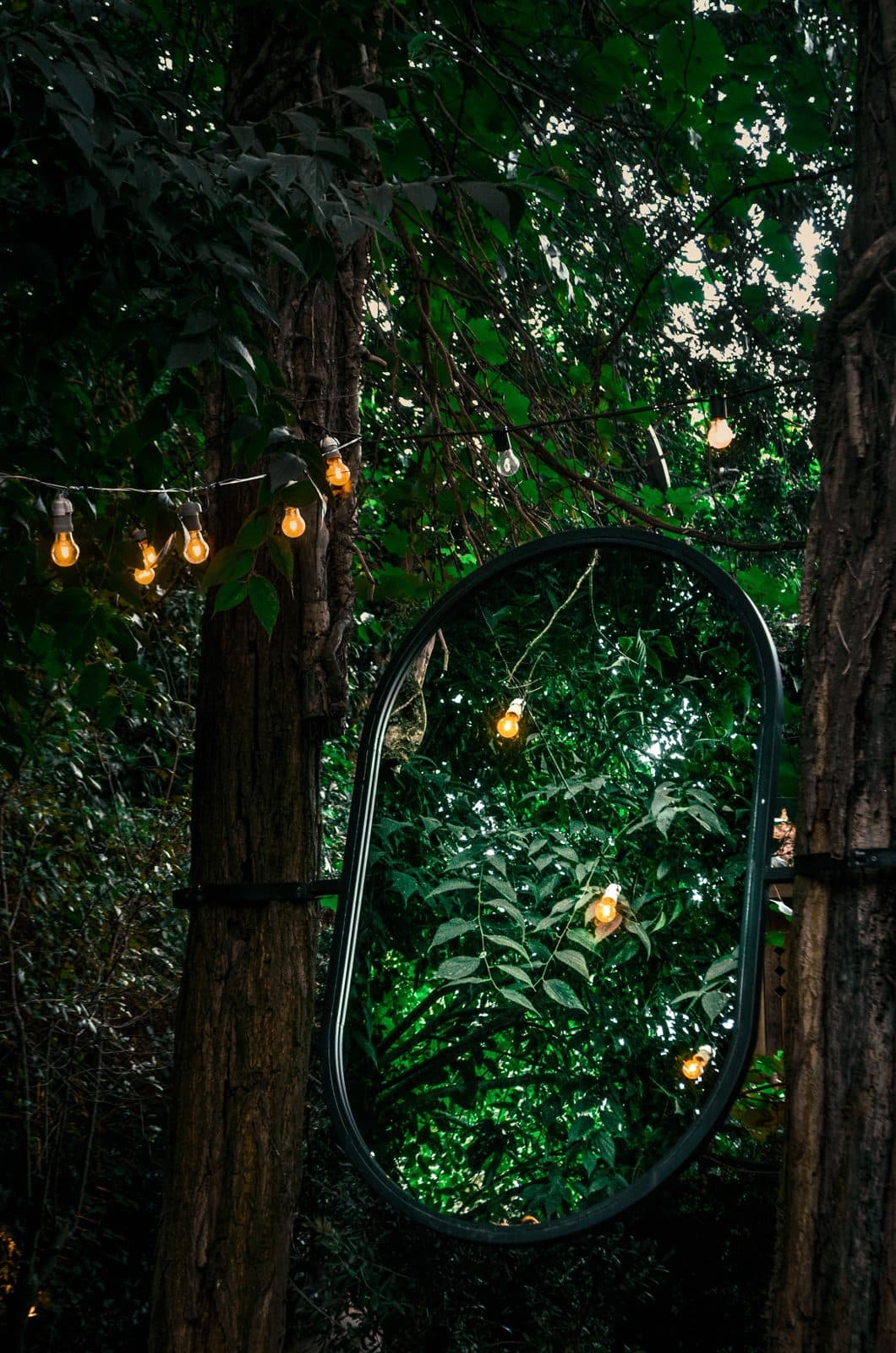 Miroir ovale dans un jardin éclairé de guirlandes