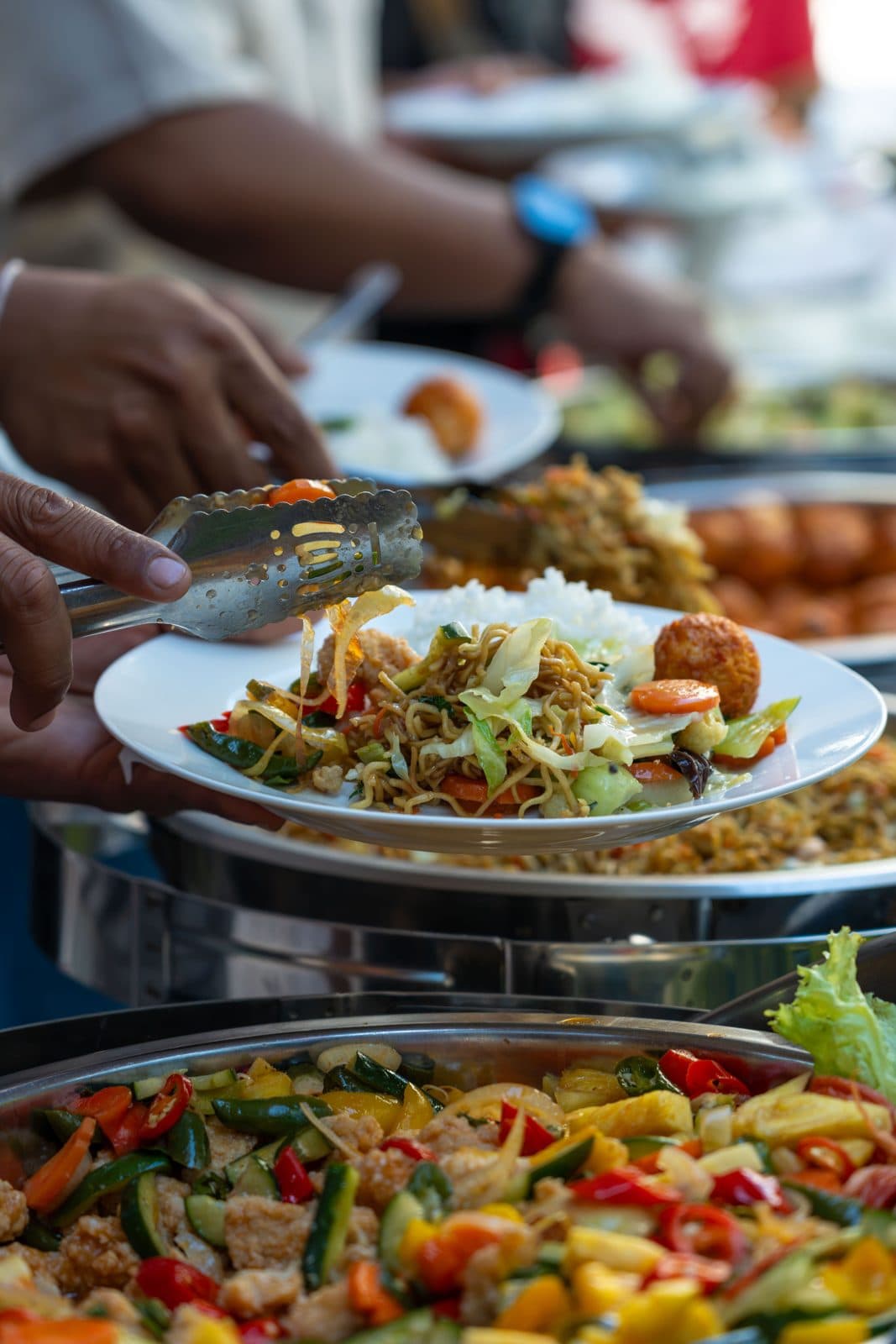 Stir-fried noodles and vegetables being served at a buffet