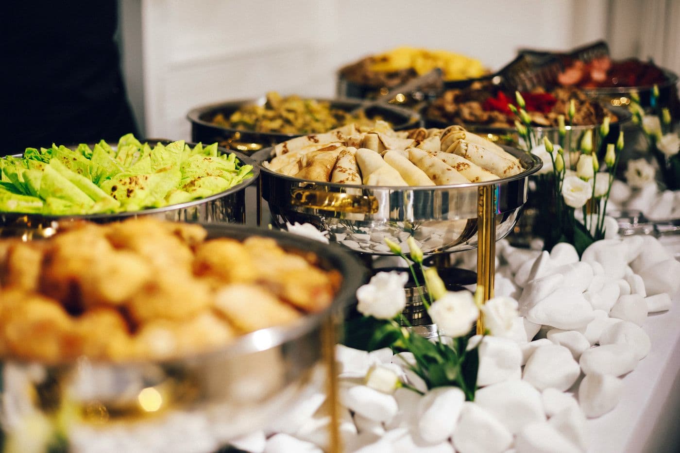 Caterer's buffet with hot dishes, crêpes and white flowers at a reception